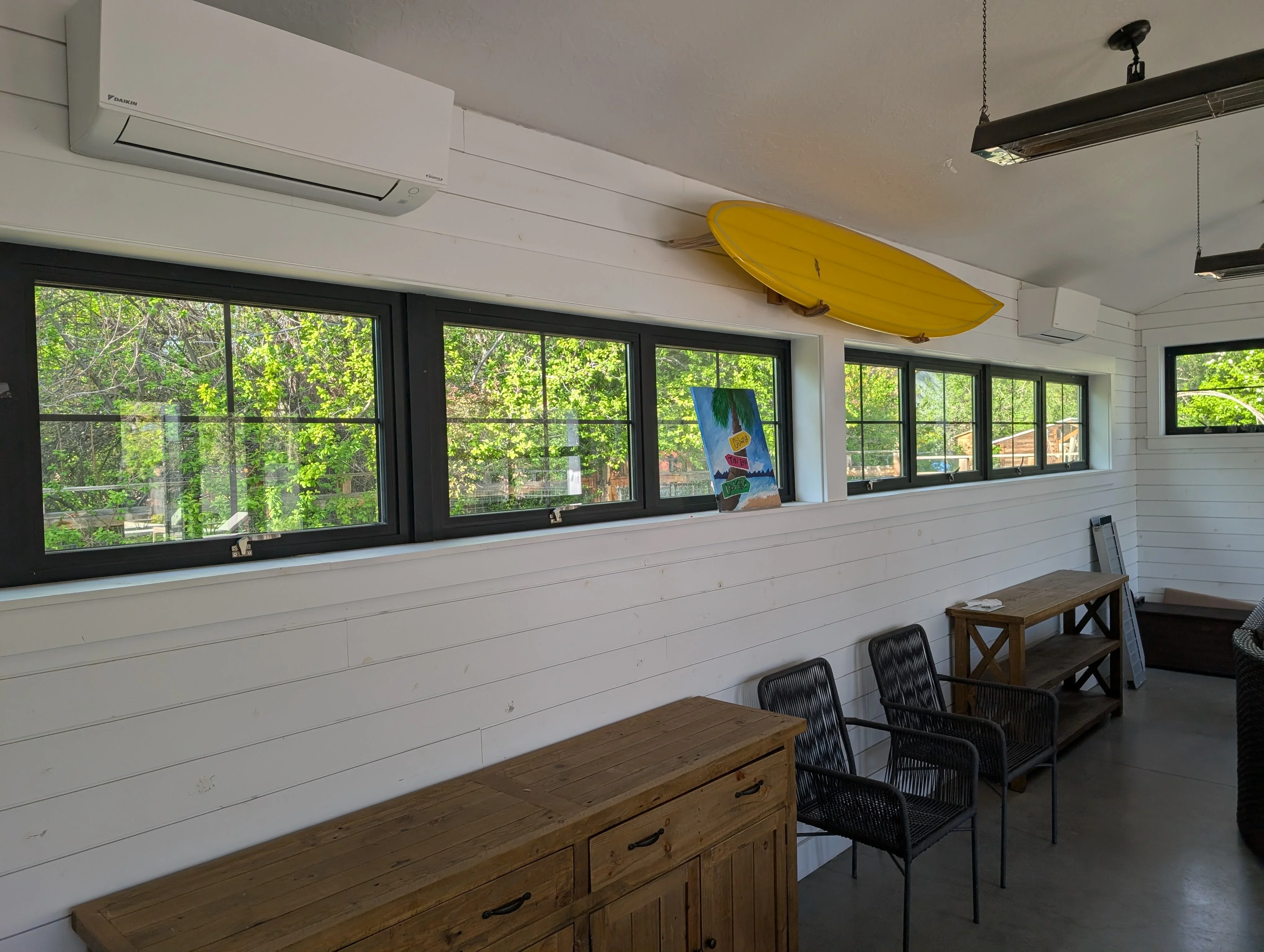 Daikin ductless mini-split HVAC units mounted on white shiplap wall in recreational room with black-framed windows