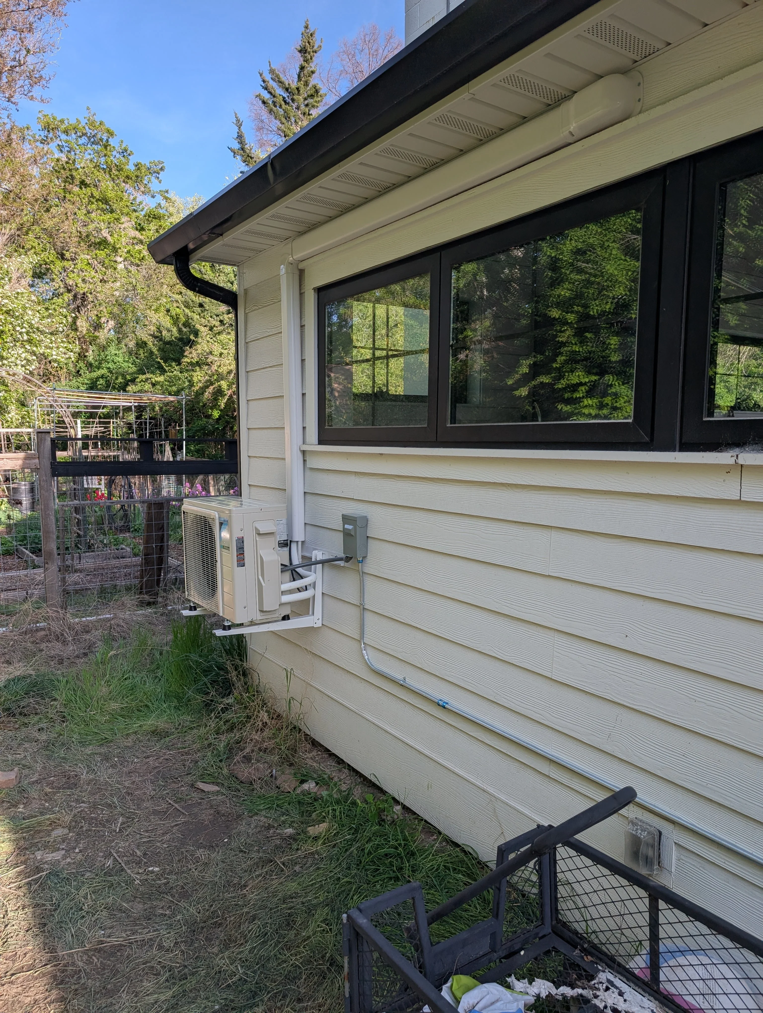 Exterior mini-split heat pump condenser mounted on cream siding with refrigerant lines and electrical connections