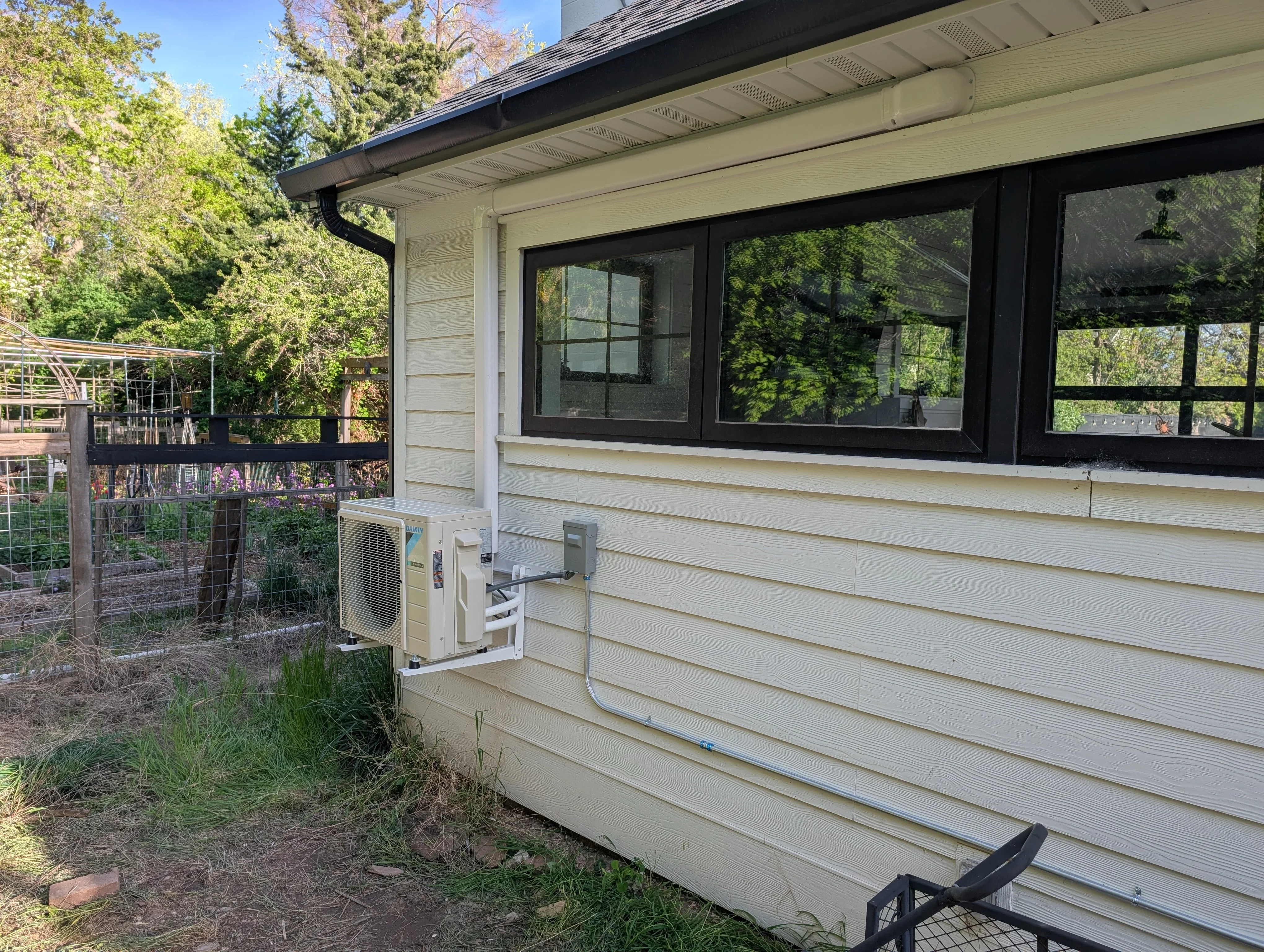 Ductless mini-split outdoor compressor unit mounted on cream siding with black refrigerant lines and electrical connections